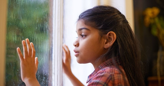 little girl looking out rain covered window