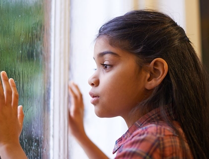 little girl looking out rain covered window